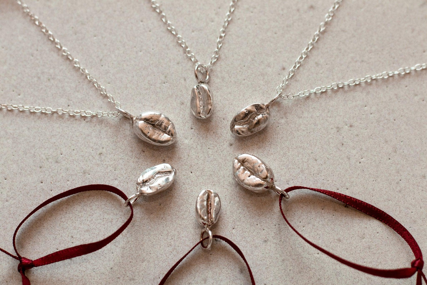 Six sterling silver coffee bean pendants are positioned in a star formation, each bean a different variety of coffee bean