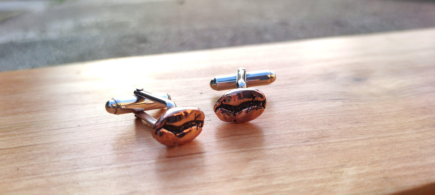 Pictured close up are two red bronze and sterling silver cuff links resting on a wooden board